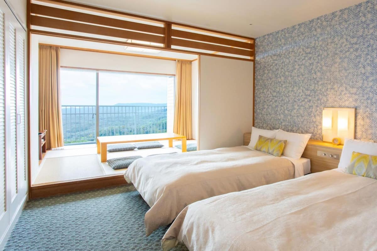 Ein Hotelzimmer mit zwei Betten, einem großen Fenster mit Blick, einer Holzbank und einer Wand mit Muster.