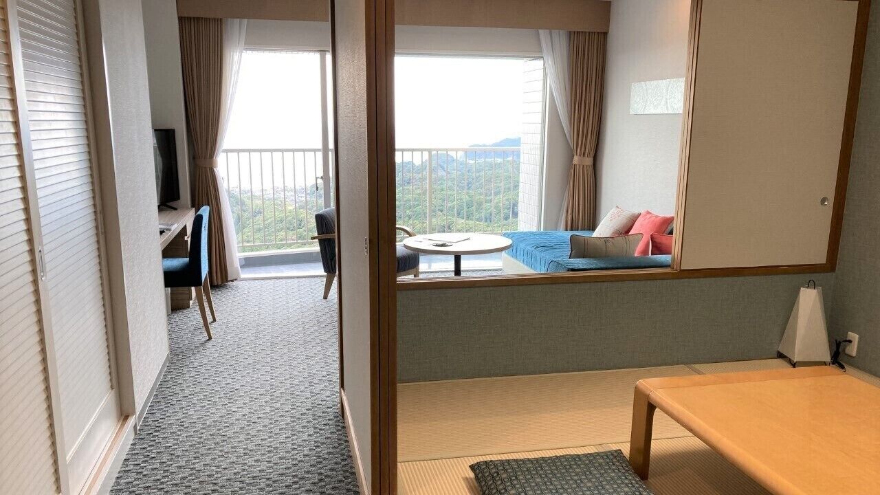 A hotel room with a balcony, a sofa, a TV, a desk, and a bed.