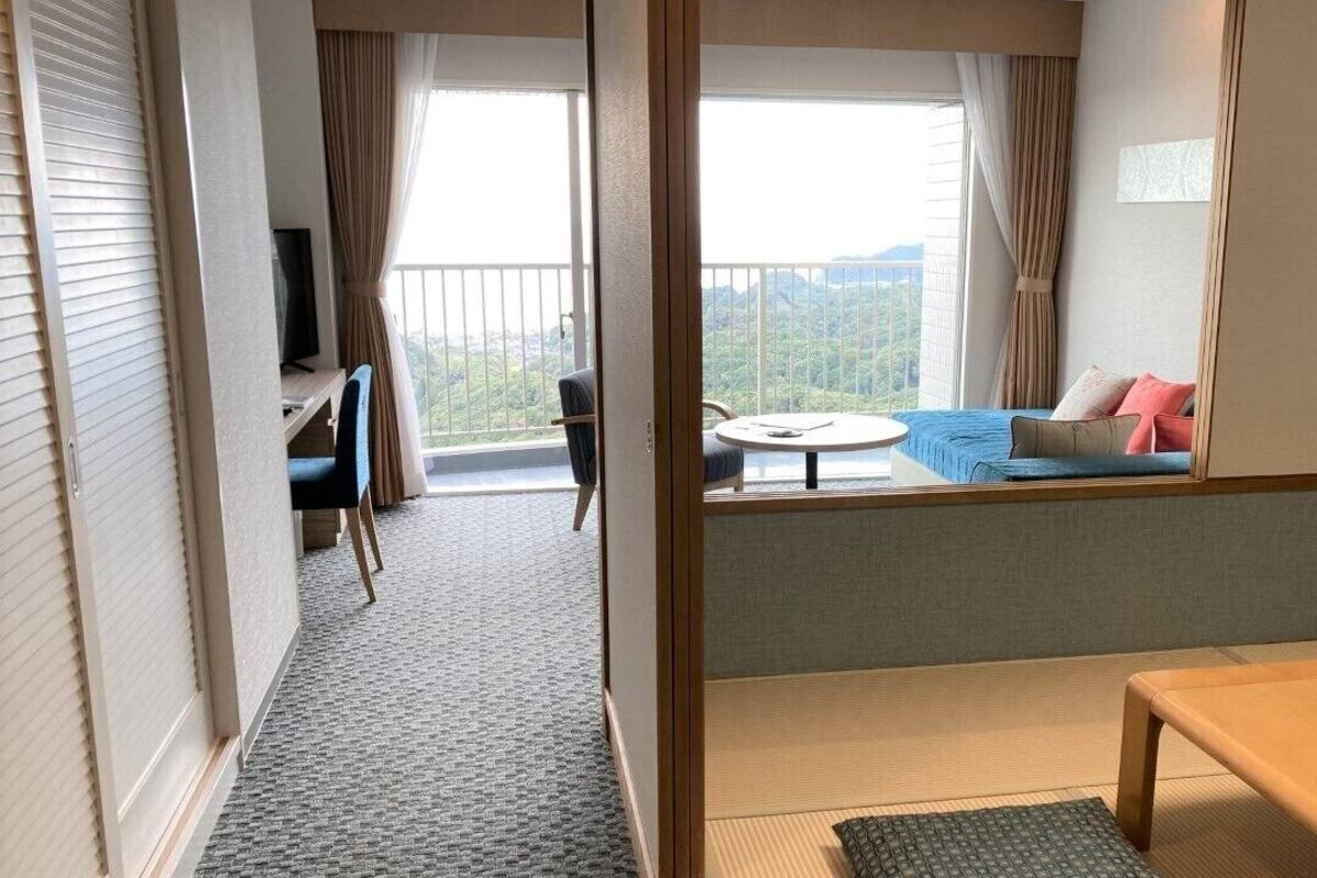 Ein Hotelzimmer mit Balkon, einer Couch, einem Fernseher, einem Schreibtisch und einem Bett.