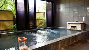 A hot tub with a view of a garden through a window, a small wooden structure, and a tiled wall.