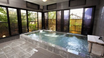 Un ambiente tipo spa con una bañera de hidromasaje, ventanas amplias y vistas a una valla de madera y árboles.