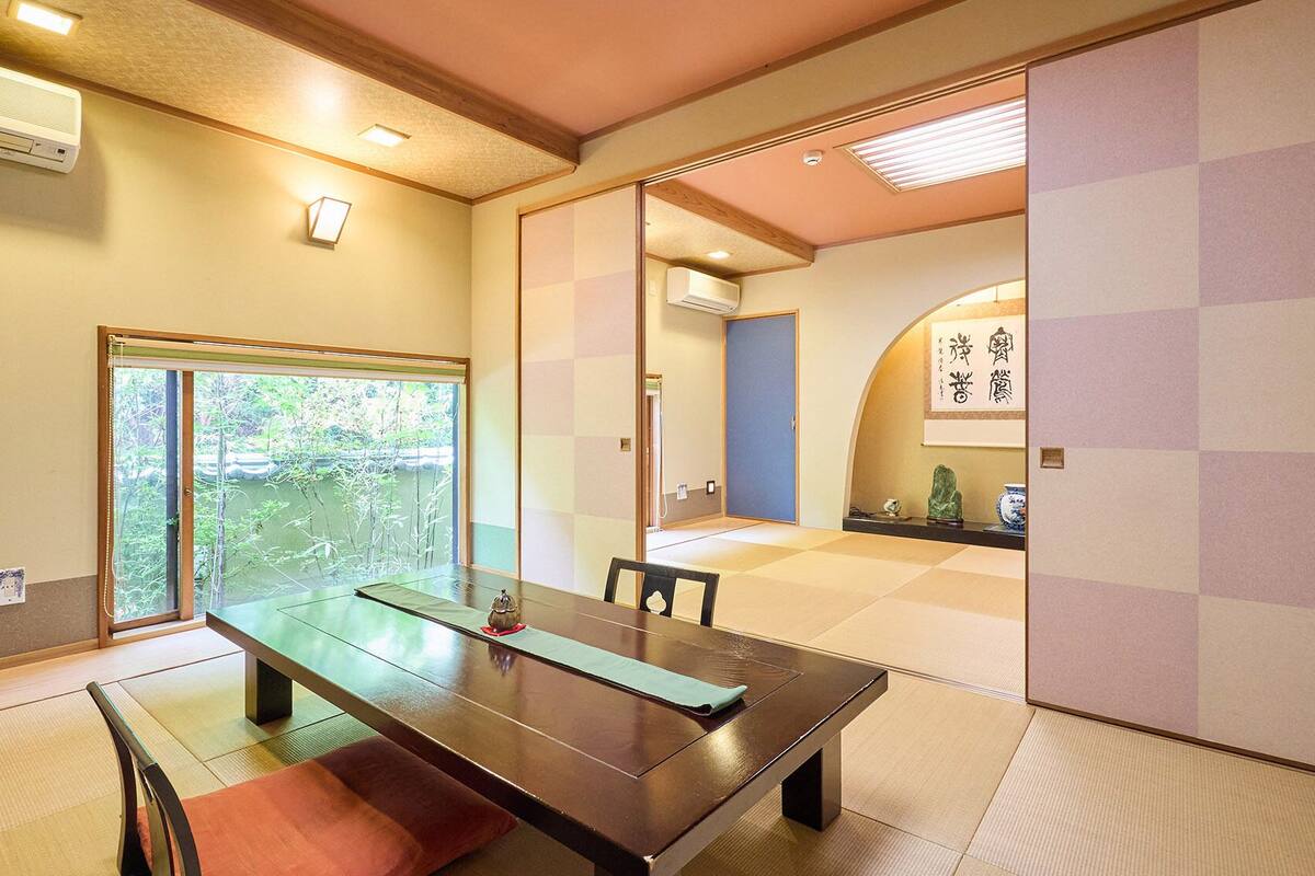 Een traditionele Japanse kamer met tatami vloerbedekking, een schuifdeur, een tafel met bijbehorende mat en uitzicht op groen.