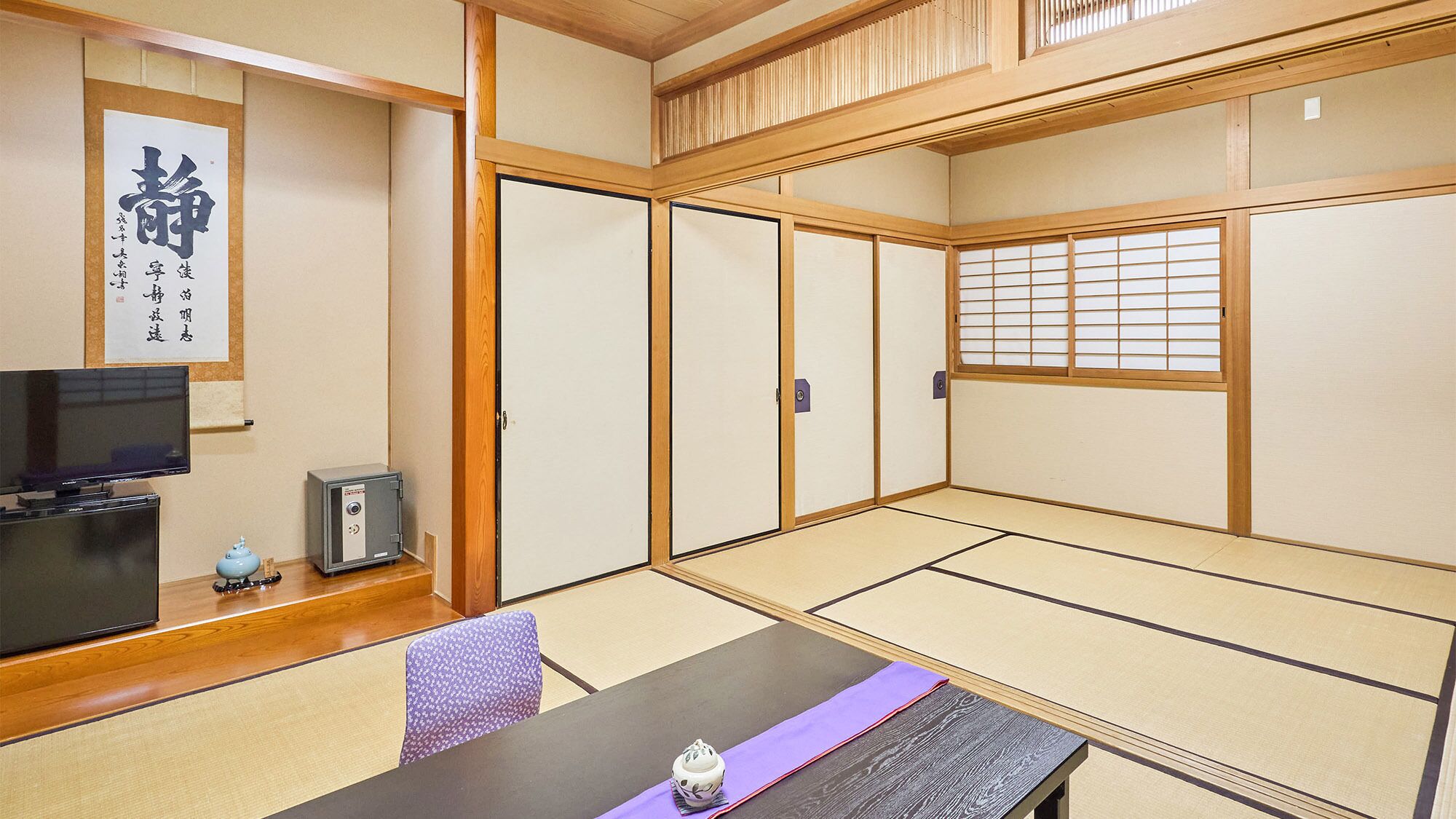 Ein traditioneller japanischer Raum mit Tatami-Böden, einem Fernseher, einem Safe und einem Shoji-Bildschirm.