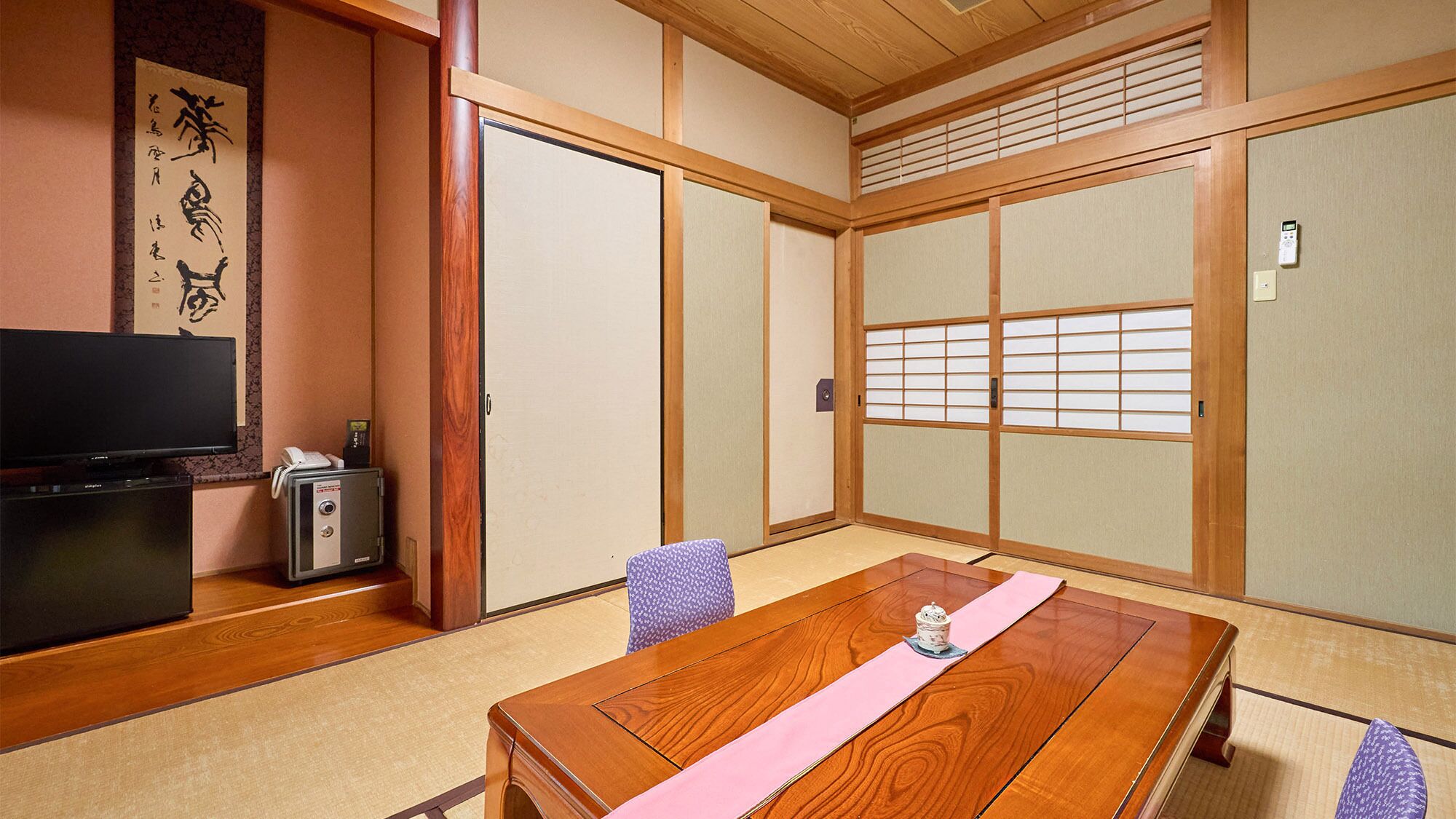 Ein traditioneller japanischer Raum mit Tatami-Boden, einem Holztisch, einem Fernseher und Schiebetüren.