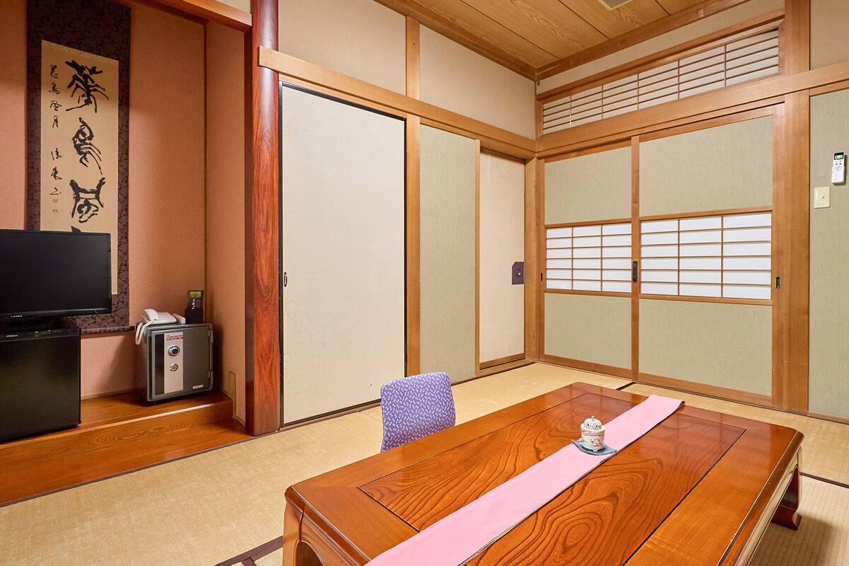Een traditionele Japanse kamer met tatami vloerbedekking, een houten tafel, een televisie en schuifdeuren.