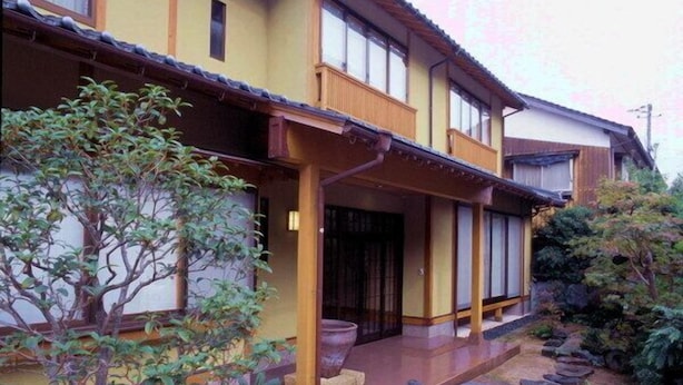 A traditional Japanese house with a wooden porch, a potted plant, and a stone pathway.