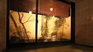 A room with a large window overlooking a garden with various plants and a bench.