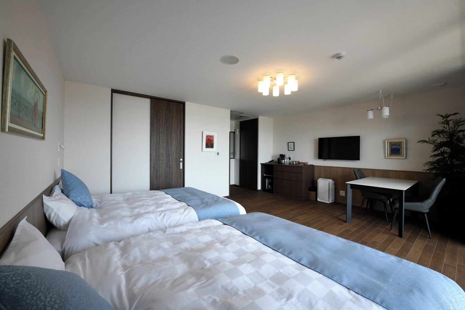 Una habitación de hotel con dos camas, un escritorio, una silla, un televisor y una kitchenette.