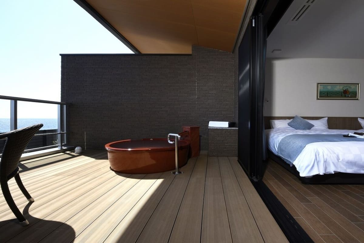 A balcony with a hot tub, a bed with pillows, and a painting on the wall.