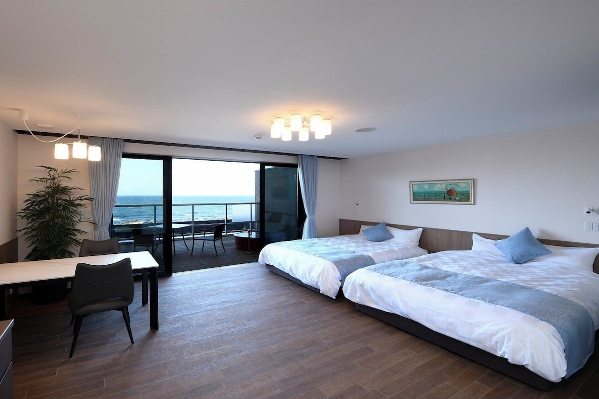 A hotel room with a balcony, a desk, two beds, and a TV.