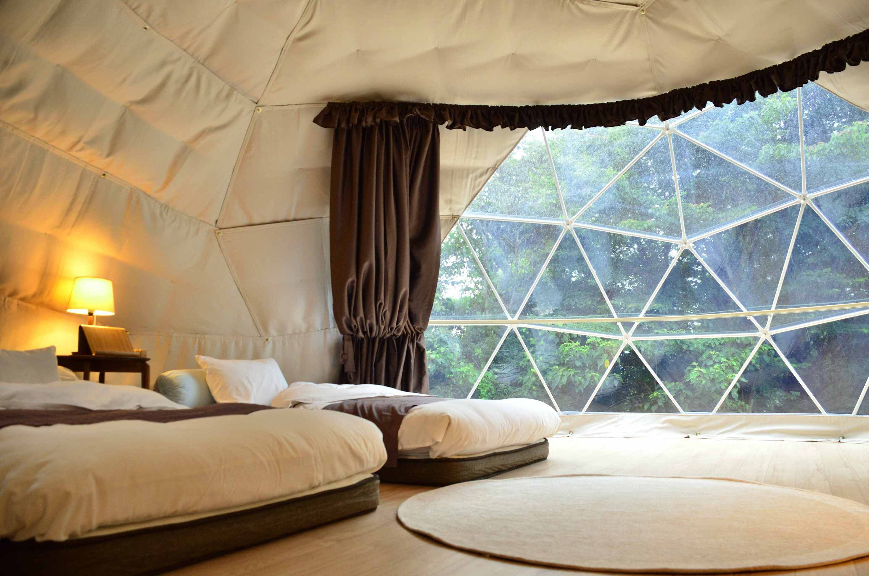 A tent-style room with two beds, a nightstand, and a large window with a geometric view.