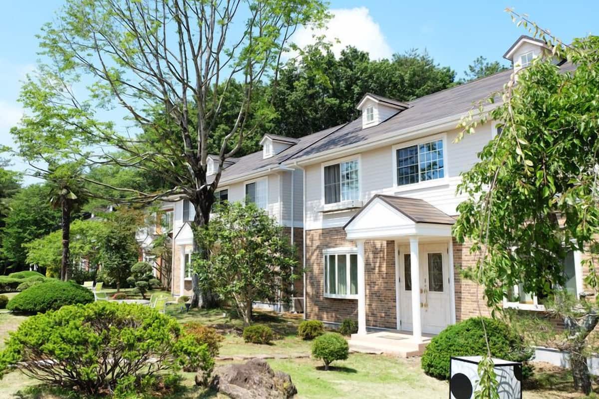 Une maison à deux étages avec une façade en briques, des éléments décoratifs blancs et un porche à l’avant.
