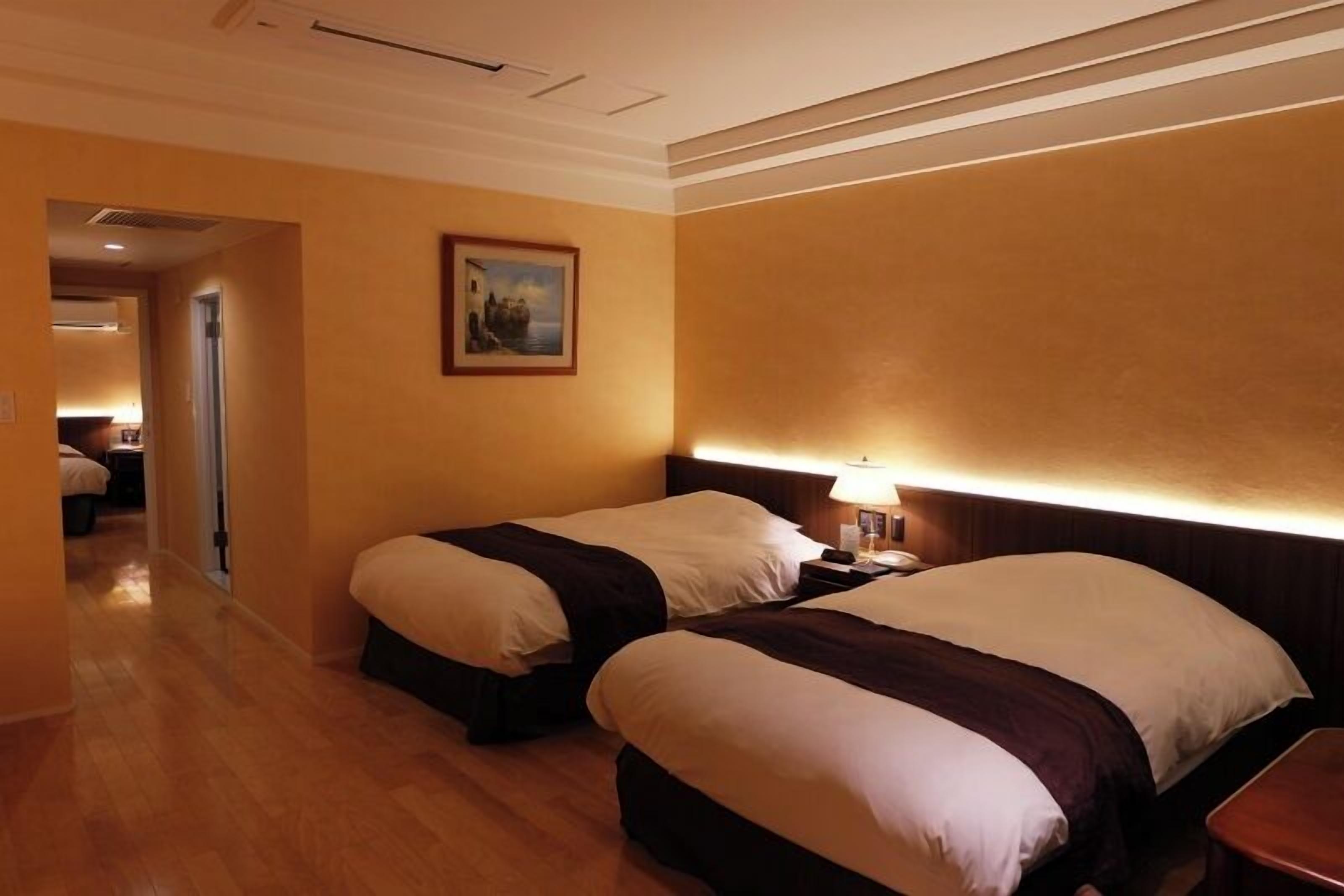 A hotel room with two beds, a nightstand, a lamp, and a painting on the wall.