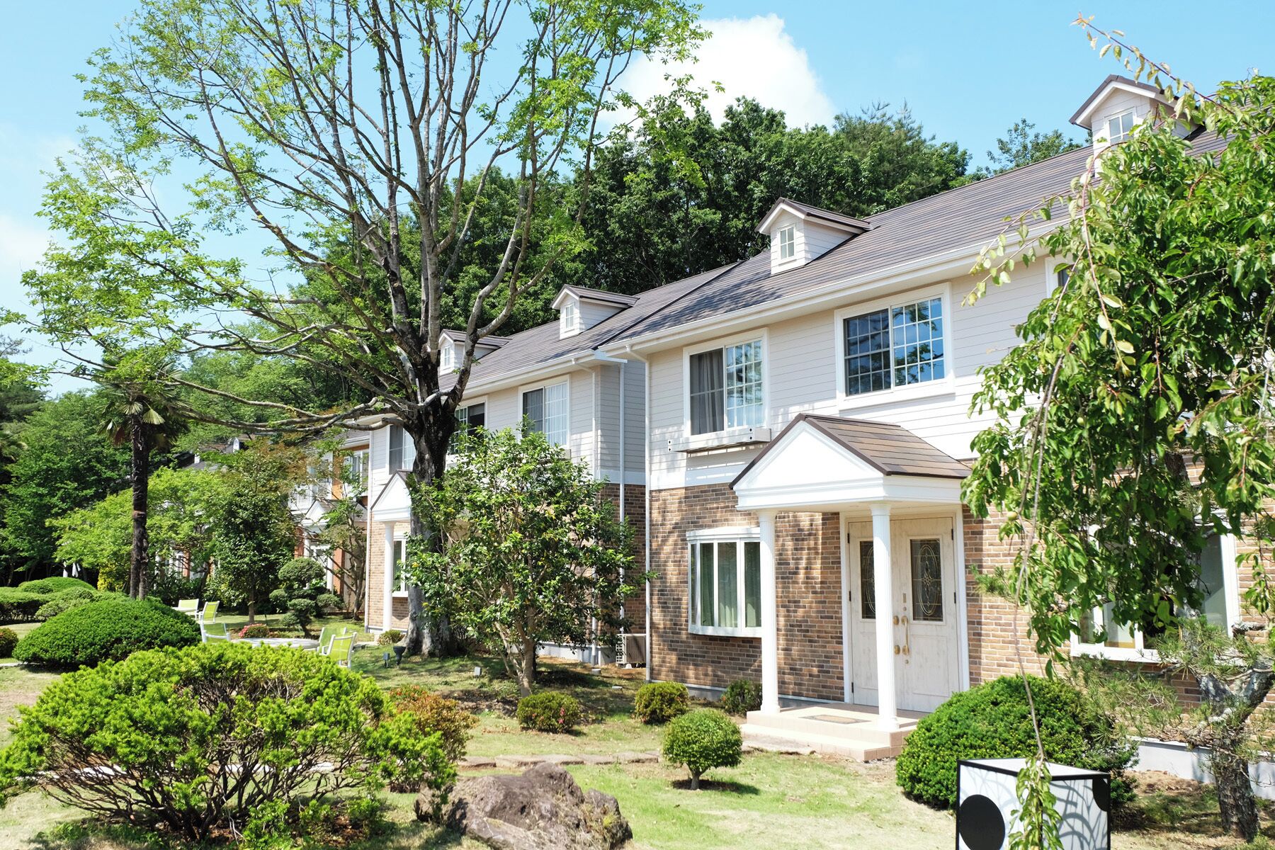 A two-story house with a well-maintained garden, a large tree, and a brick exterior.