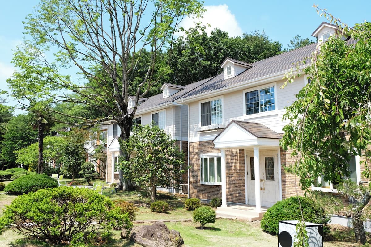 Une maison à deux étages avec un jardin bien entretenu, un grand arbre et une façade en briques.