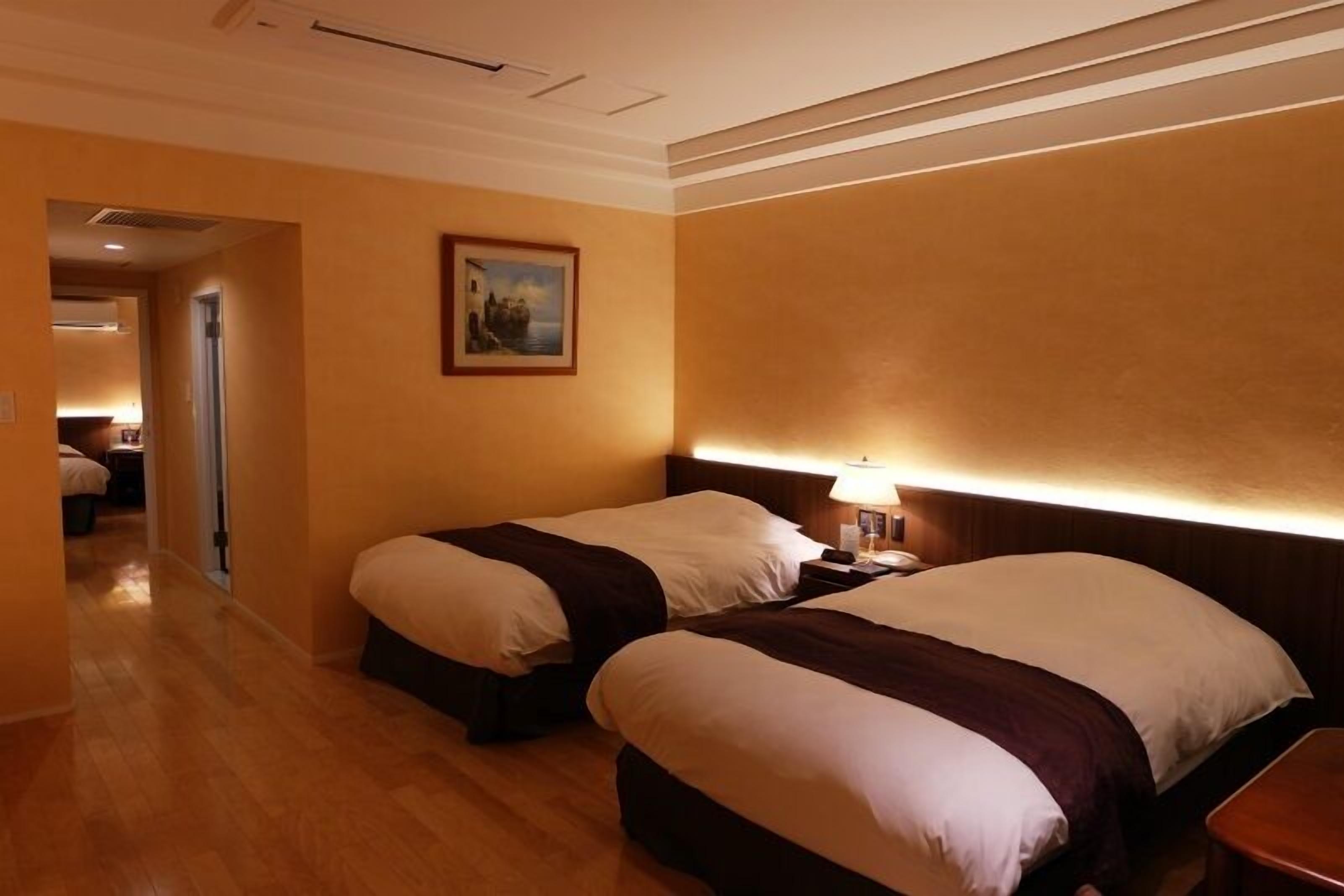 Habitació d'hotel amb dos llits, una taula de nit amb una làmpada, un quadre a la paret i un sòl de fusta.