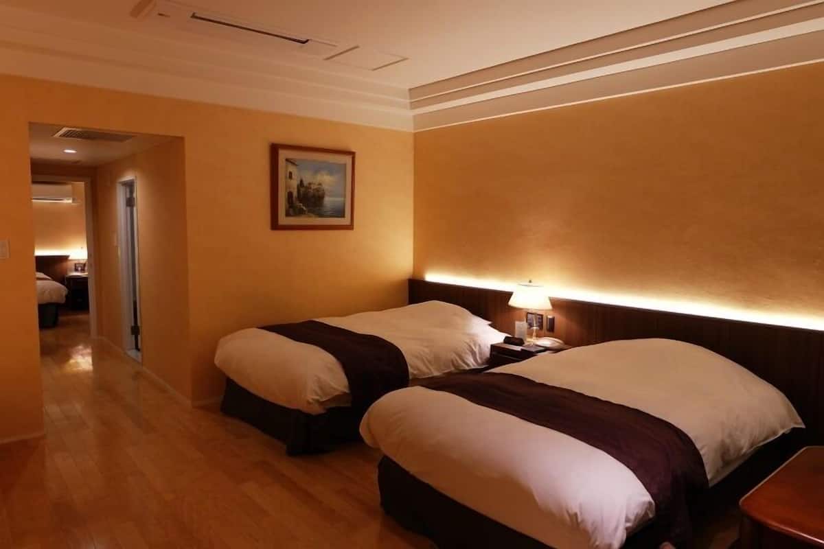 Une chambre d’hôtel avec deux lits, une table de chevet avec une lampe, un tableau au mur et un plancher en bois.