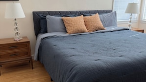 A neatly made bed with a grey blanket, a wooden nightstand with a lamp, and a framed picture on the wall. - Charming 1-bedroom house in convenient Burbank with AC (Burbank)
