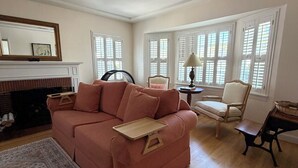 A living room with a pink sofa, a wooden coffee table, a wicker chair, and a side table with a lamp. - Charming 1-bedroom house in convenient Burbank with AC (Burbank)