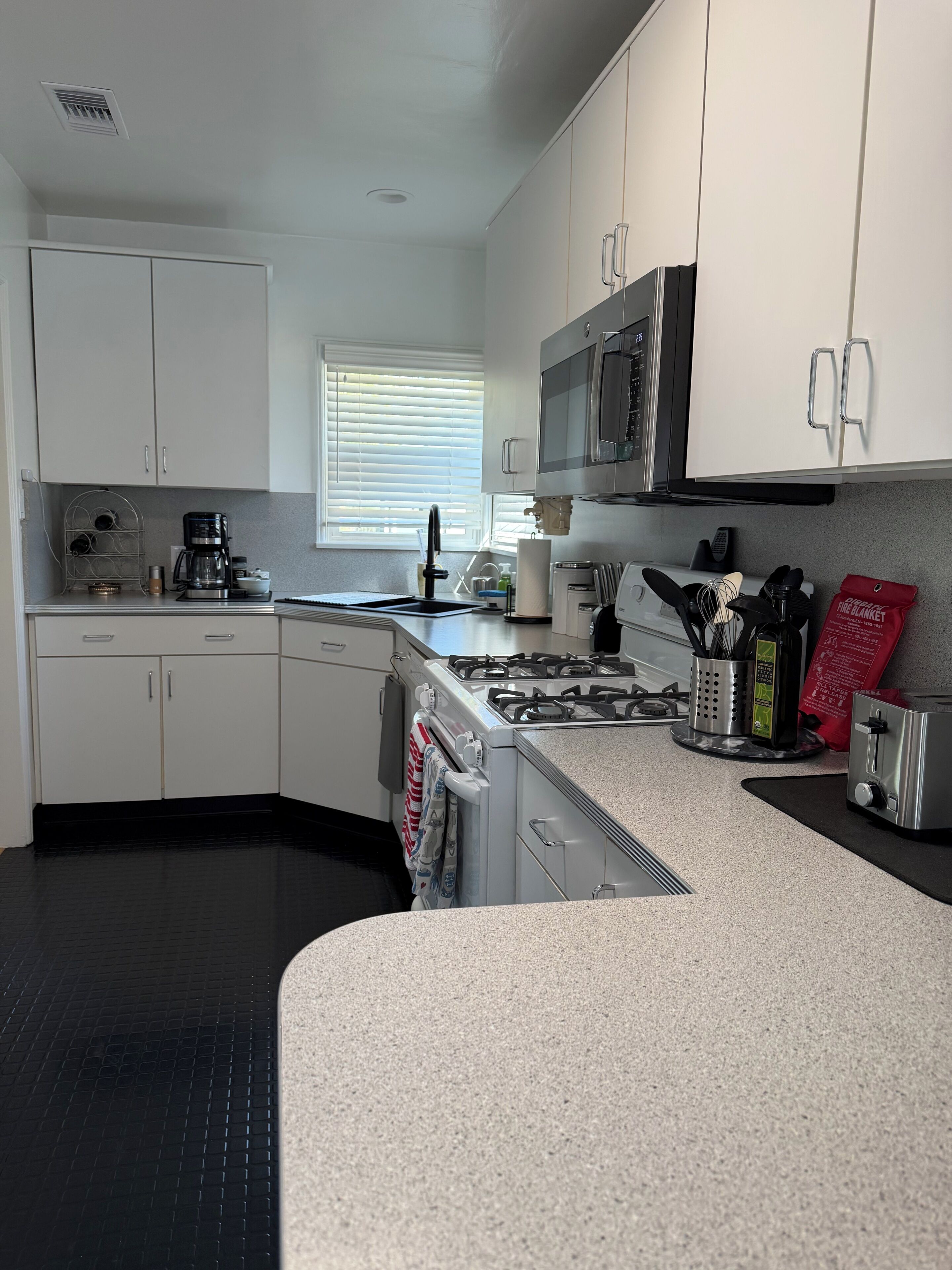 A kitchen with white cabinets, a microwave, a gas stove, and a coffee maker.