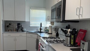 A kitchen with white cabinets, a microwave, a gas stove, and a coffee maker. - Charming 1-bedroom house in convenient Burbank with AC (Burbank)