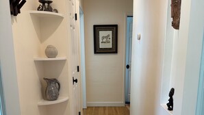 A hallway with white walls, wooden flooring, and shelves with various decorative items. - Charming 1-bedroom house in convenient Burbank with AC (Burbank)