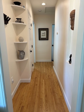 A hallway with white walls, wooden flooring, and shelves with various decorative items. - Charming 1-bedroom house in convenient Burbank with AC (Burbank)