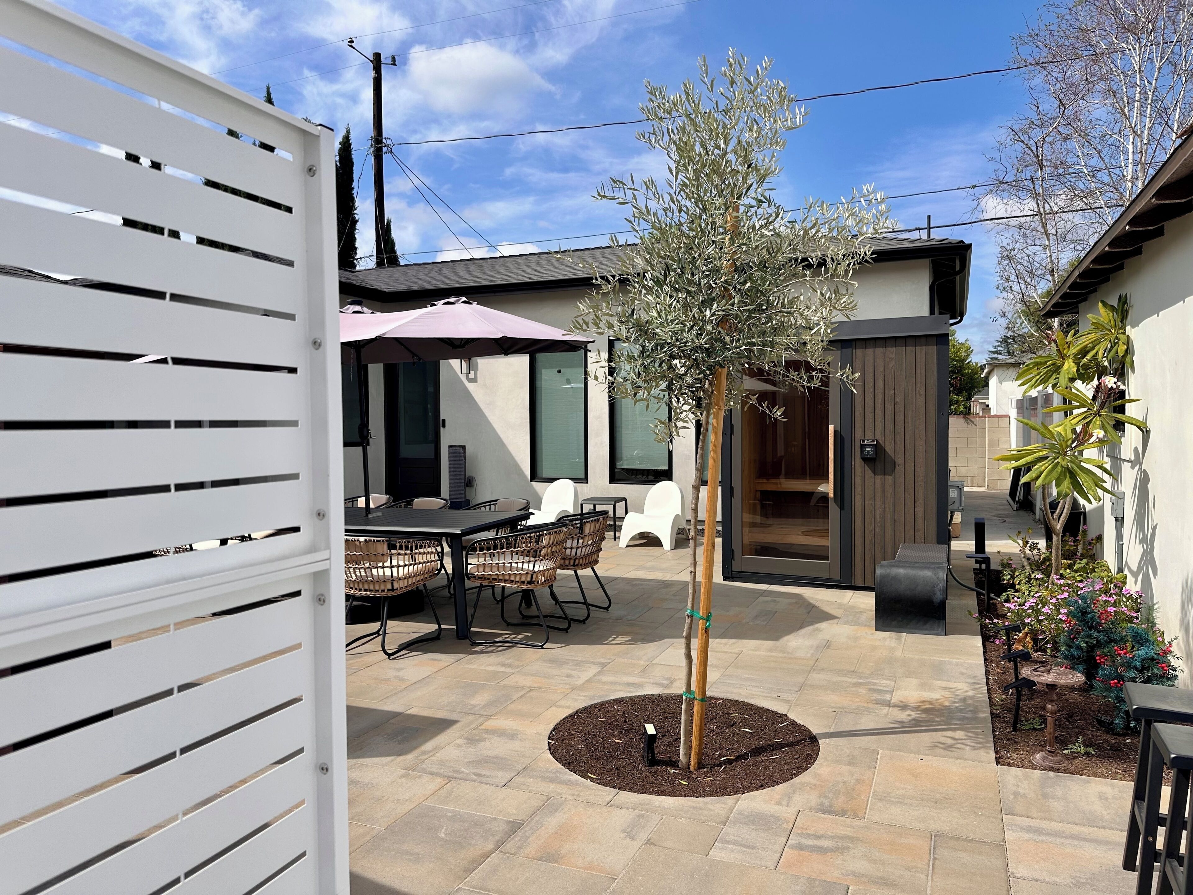 Un espace patio comprenant une table et des chaises, un petit arbre et un coin salon abrité.