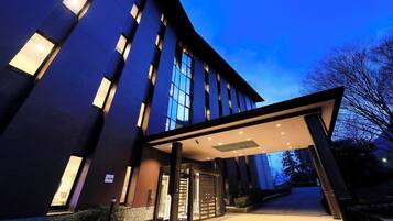 A modern hotel entrance with a covered walkway, large windows, and a well-lit facade.