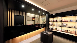 A modern reception area with a black reception desk, a flat-screen TV, a decorative wall panel, and a display case with various items. - Point Vacation Kaga Yamanaka (Kaga)