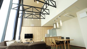 A modern hotel room with a large window, a flat-screen TV, a dining area with a table and chairs, and a ceiling with exposed beams and pendant lights. - Point Vacation Kaga Yamanaka (Kaga)