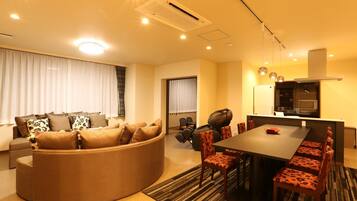 A modern living room with a sofa, dining table, chairs, and a kitchen area with a microwave.