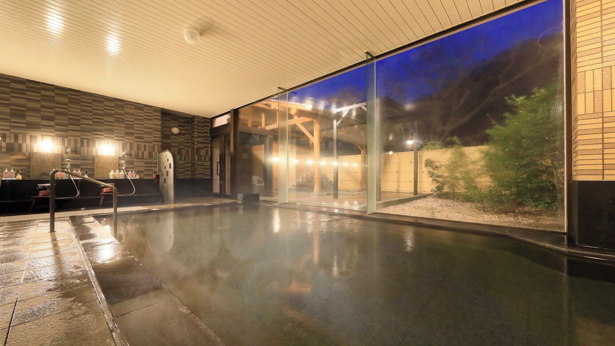 A modern lobby with a wet floor, a reception desk, and a glass wall with a view of the night outside.