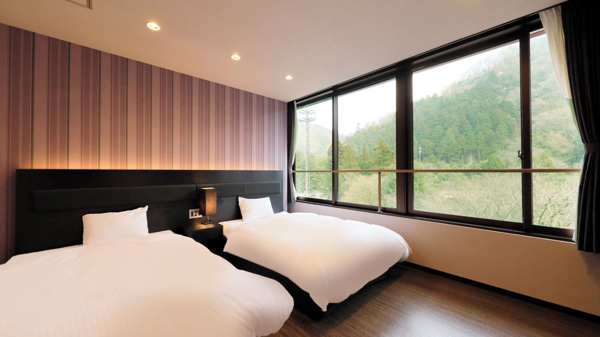 A hotel room with two beds, a large window with a forest view, and a striped wall.