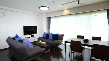 A modern living room with a flat-screen TV, sofa, coffee table, and dining table with chairs.