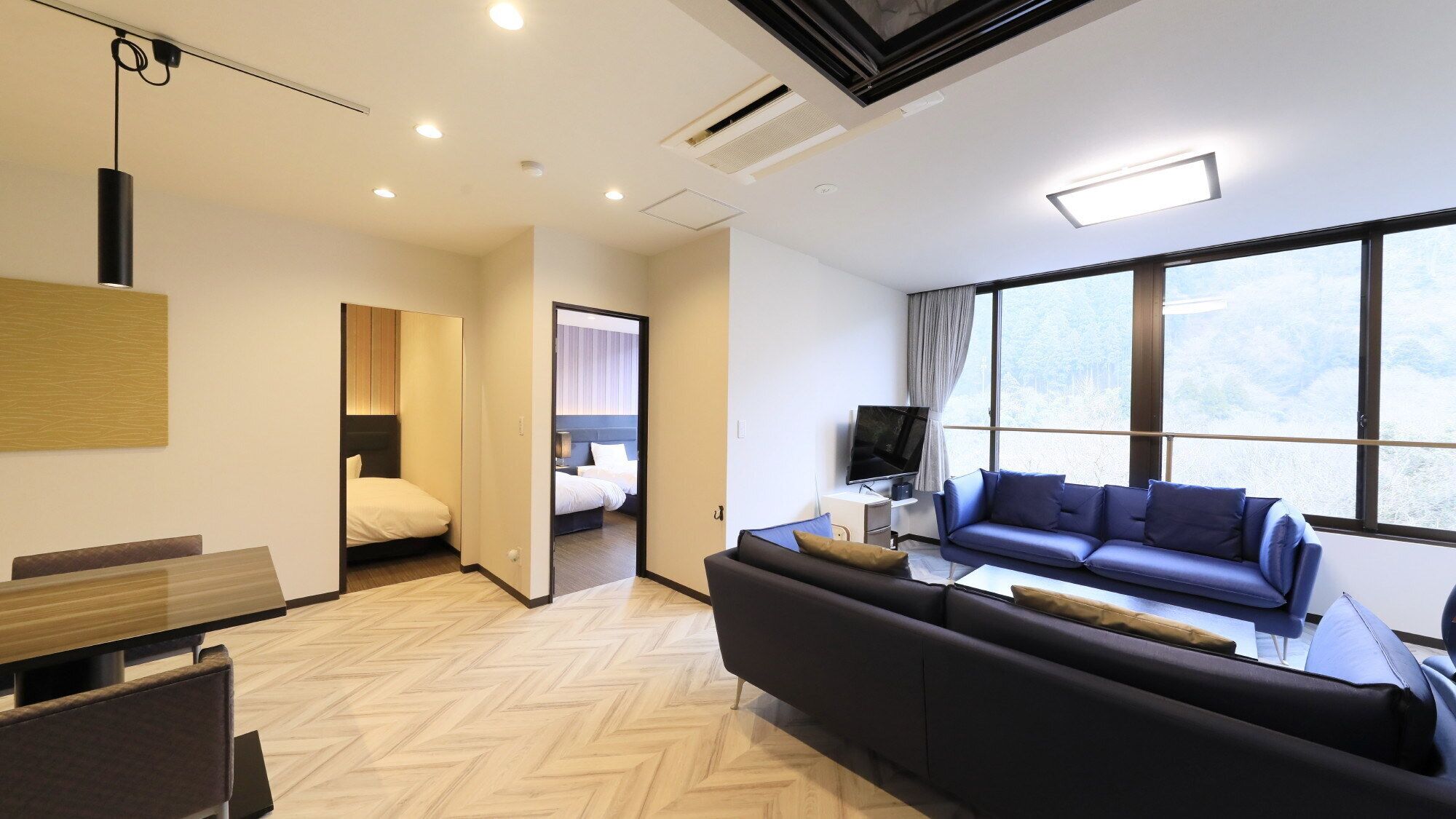 A modern hotel room with a sofa, TV, and large windows.