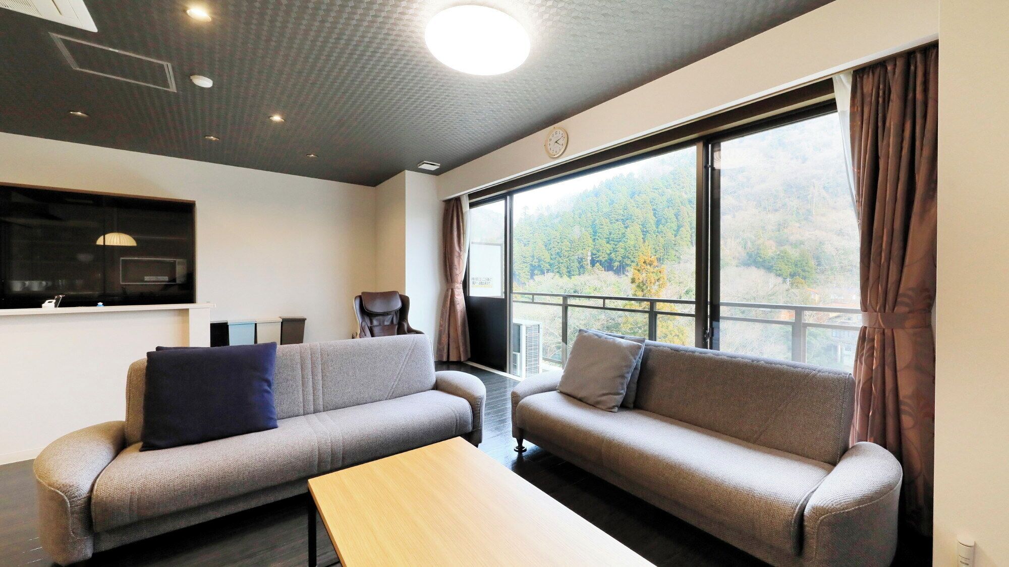 A modern room with two sofas, a wooden table, a TV, and a large window with a view of trees.