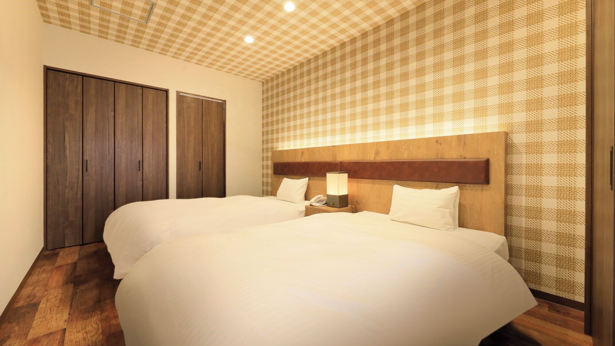 A hotel room with two beds, a wooden headboard, a checkered wall pattern, and a wooden floor.