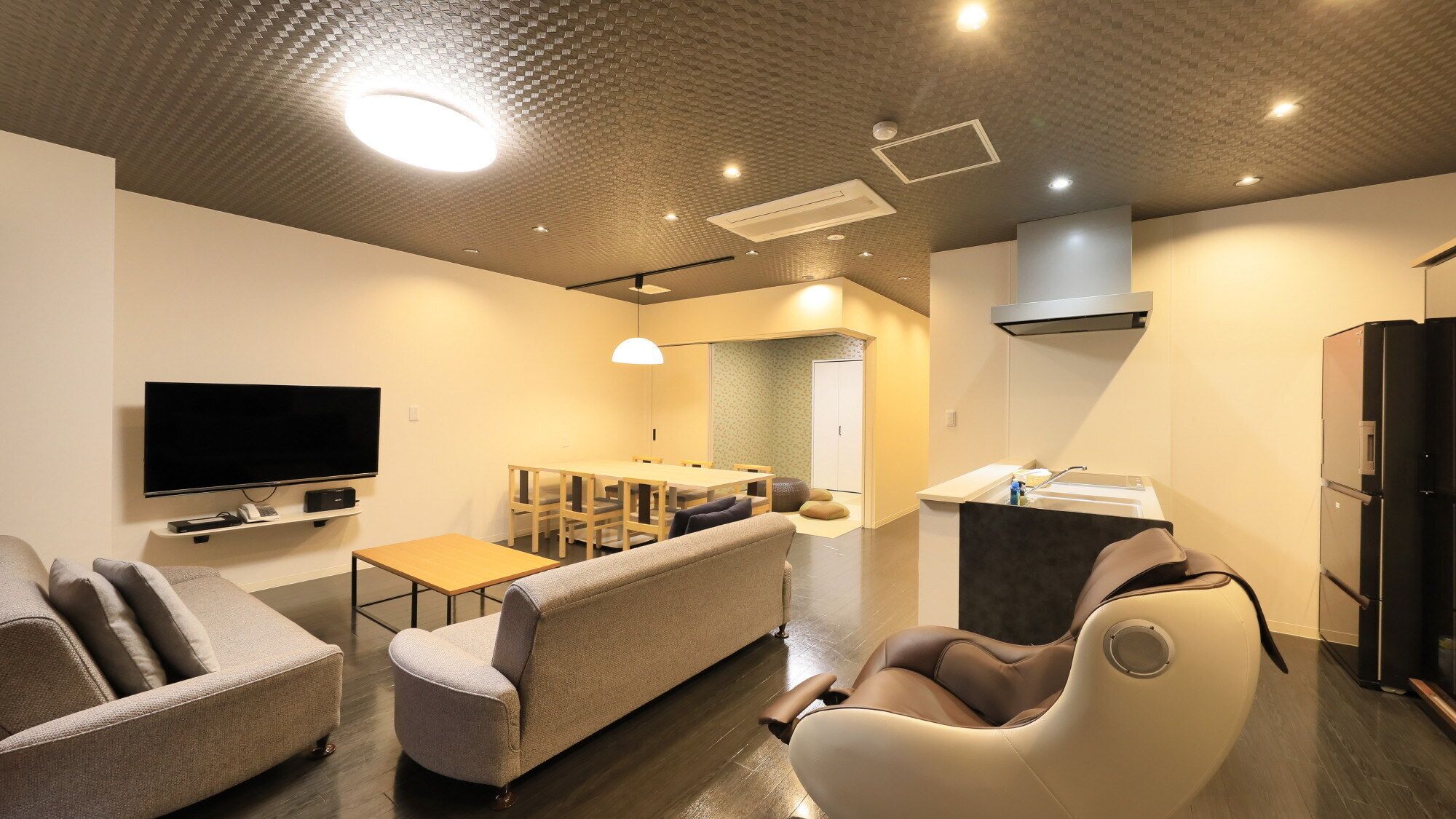 A modern living room with a flat-screen TV, sofa, armchair, and a dining area with a table and chairs.