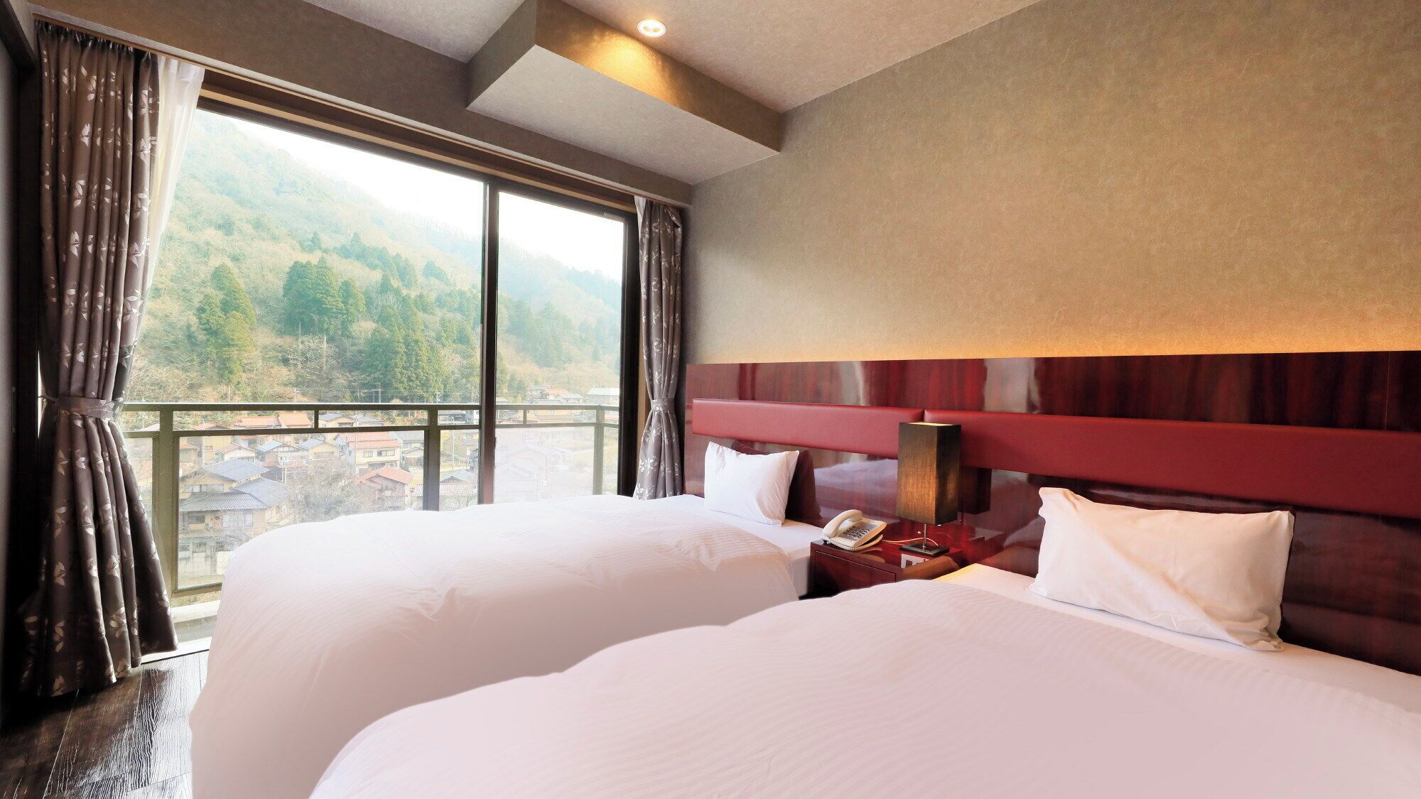 A hotel room with two beds, a nightstand with a lamp, and a view of a mountainous landscape.