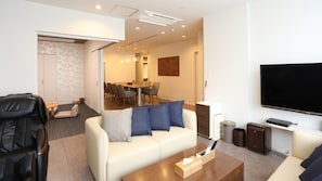 A modern living room with a sofa, coffee table, TV, and a dining area in the background. - Point Vacation Kaga Yamanaka (Kaga)