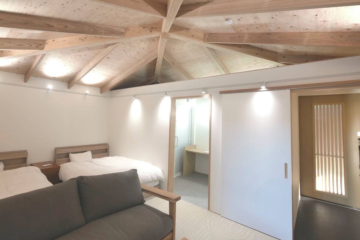 A bedroom with a sloped ceiling, a bed, a sofa, and a sliding door.
