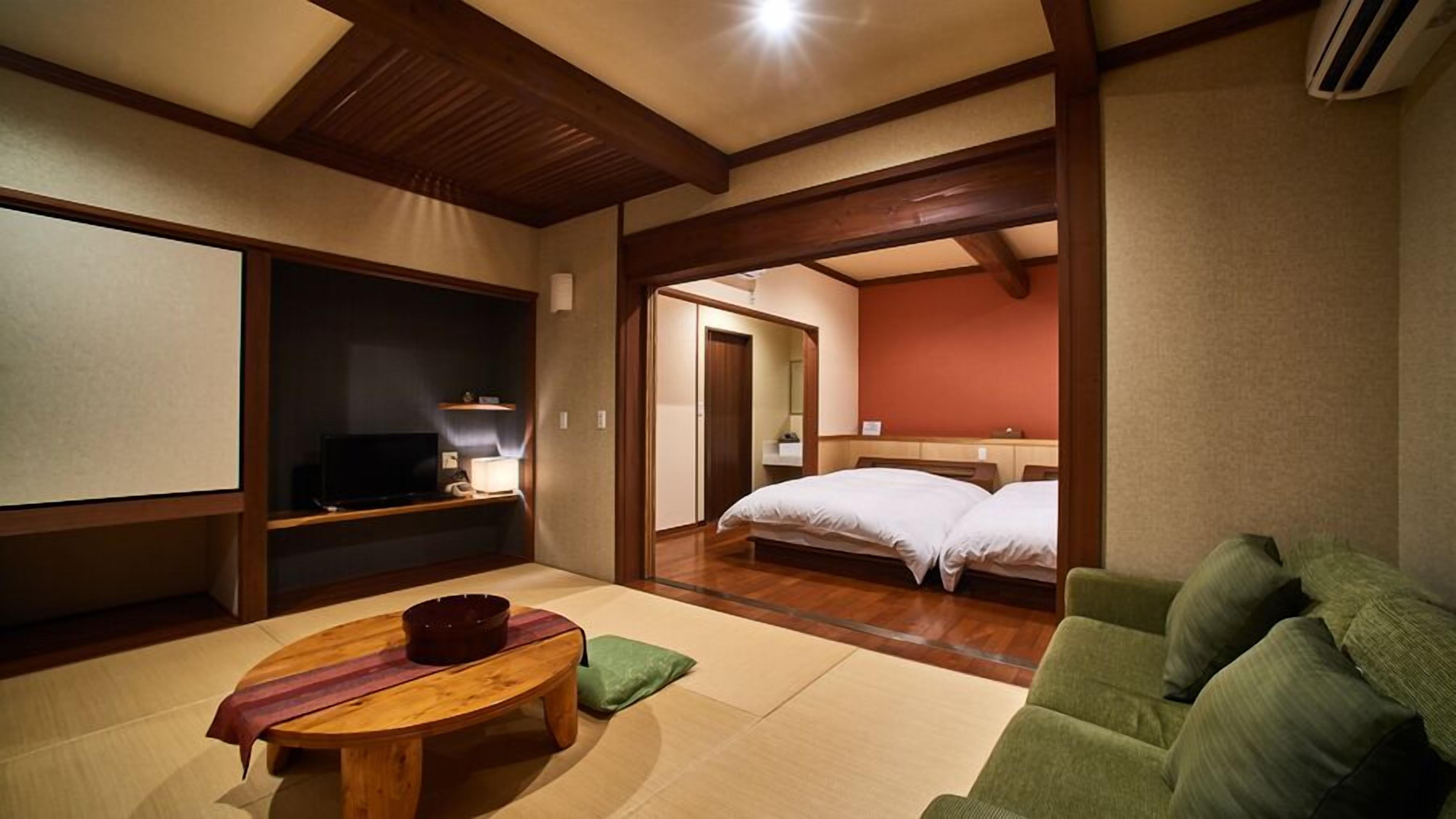Una camera d'albergo con televisione, un tavolino con una ciotola, un divano verde e un letto con due cuscini.