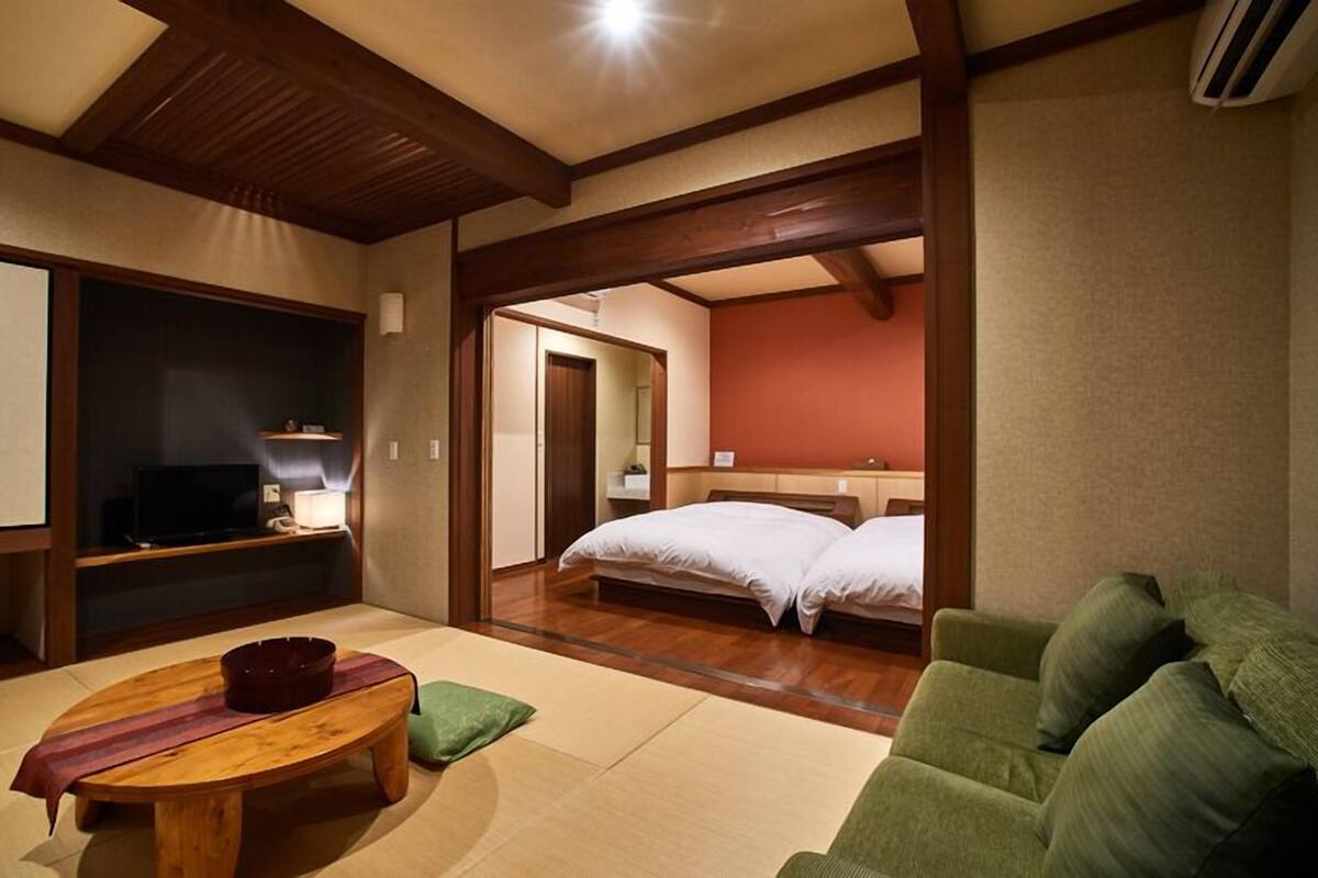 A hotel room with a television, a small table with a bowl, a green sofa, and a bed with two pillows.