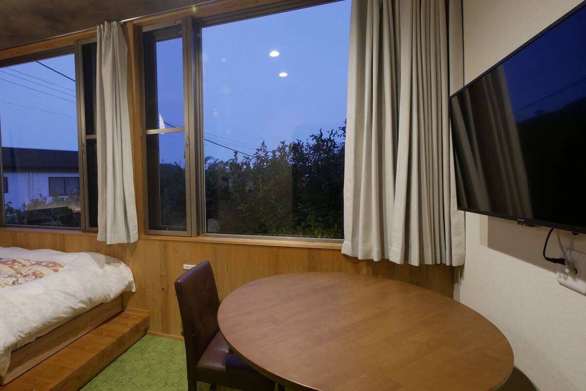 A room with two beds, a wooden table, a chair, and a TV.
