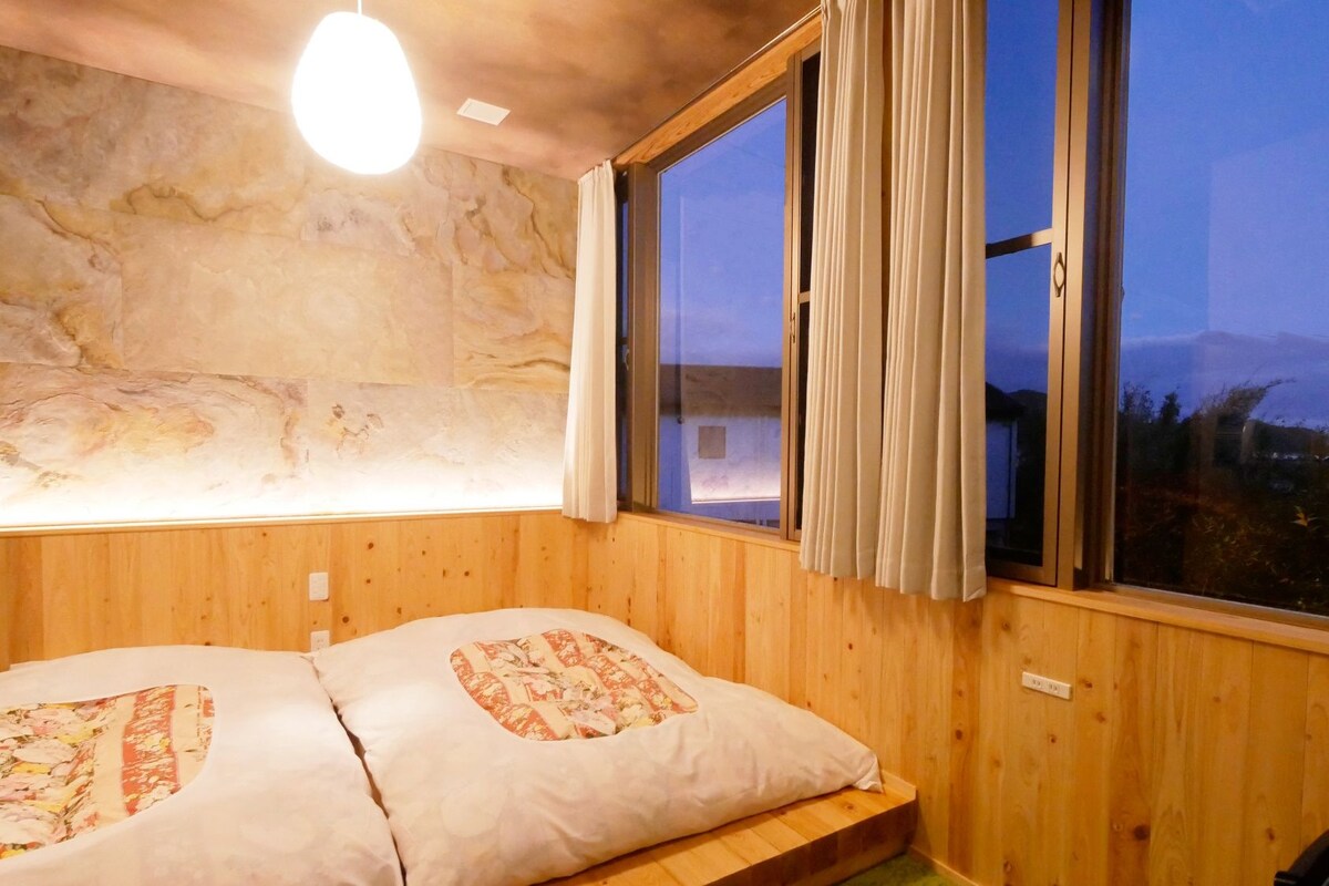 A room with wooden walls, a bed with patterned pillows, a window with curtains, and a light fixture.