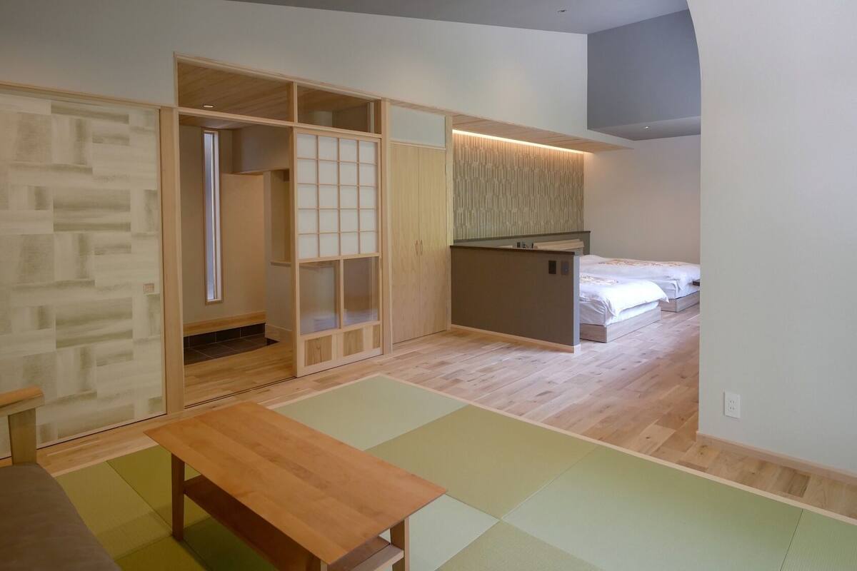 A room with a sliding door, a small kitchenette, a bed, and a wooden table.