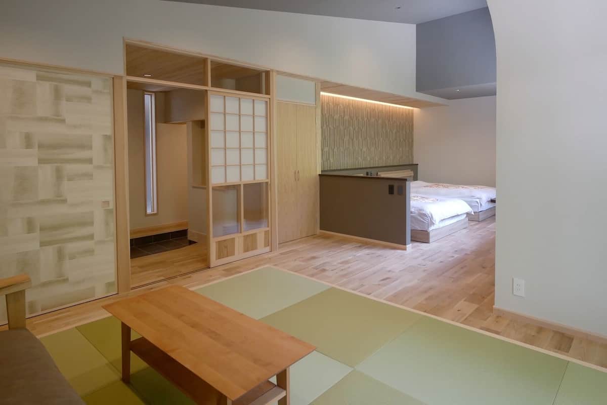 A room with a sliding door, a small kitchenette, a bed, and a wooden table.