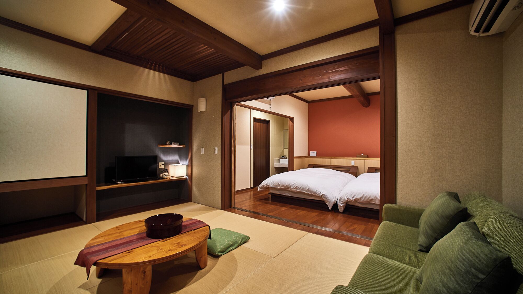 Una camera tradizionale giapponese con pavimento in tatami, un futon, una televisione e un piccolo tavolo con una ciotola.