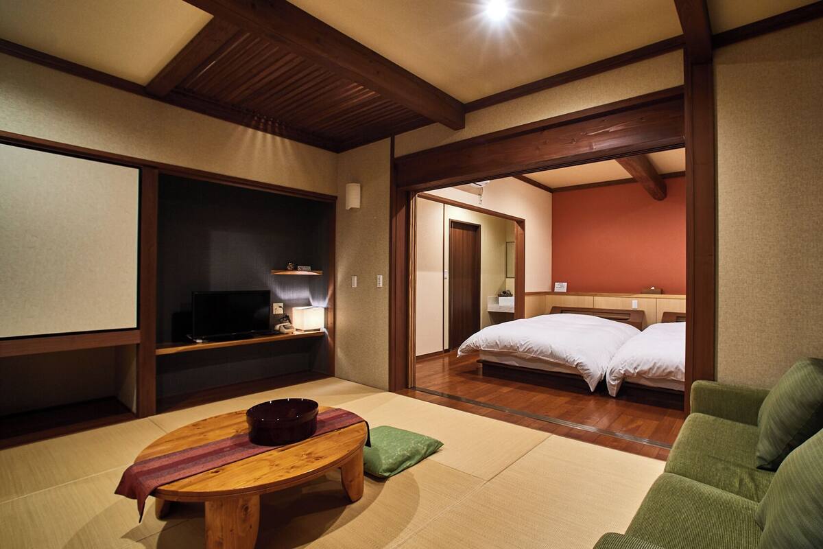 A traditional Japanese-style room with tatami flooring, a futon bed, a television, and a small table with a bowl.